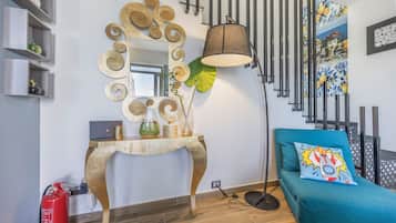 Ett modernt vardagsrum med ett konsolbord i trä, en stor spegel, en golvlampa, en soffa med en färgglad kudde och en brandsläckare.
