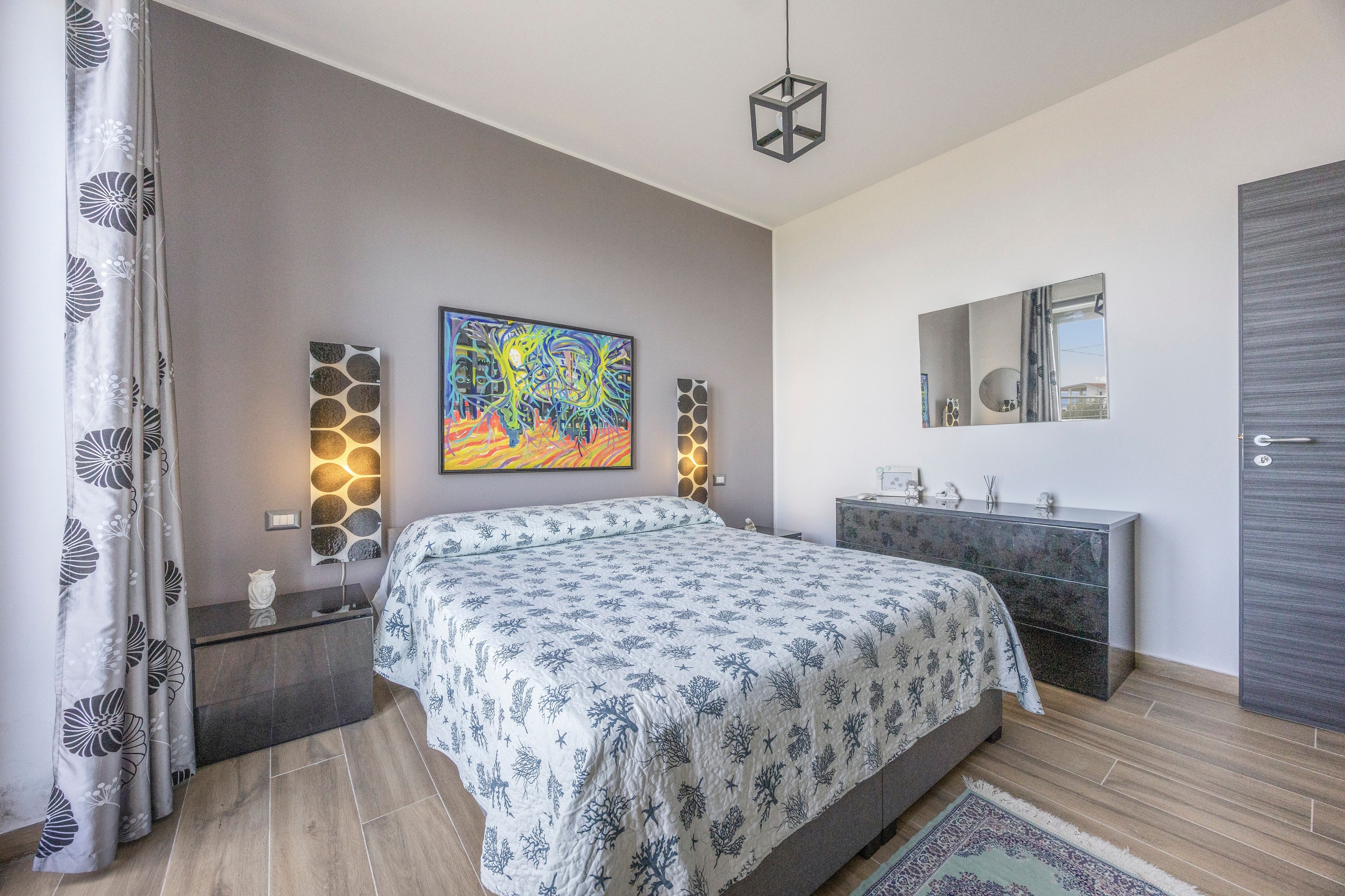 Quarto com cama, mesa de cabeceira, cômoda, espelho e um quadro na parede.