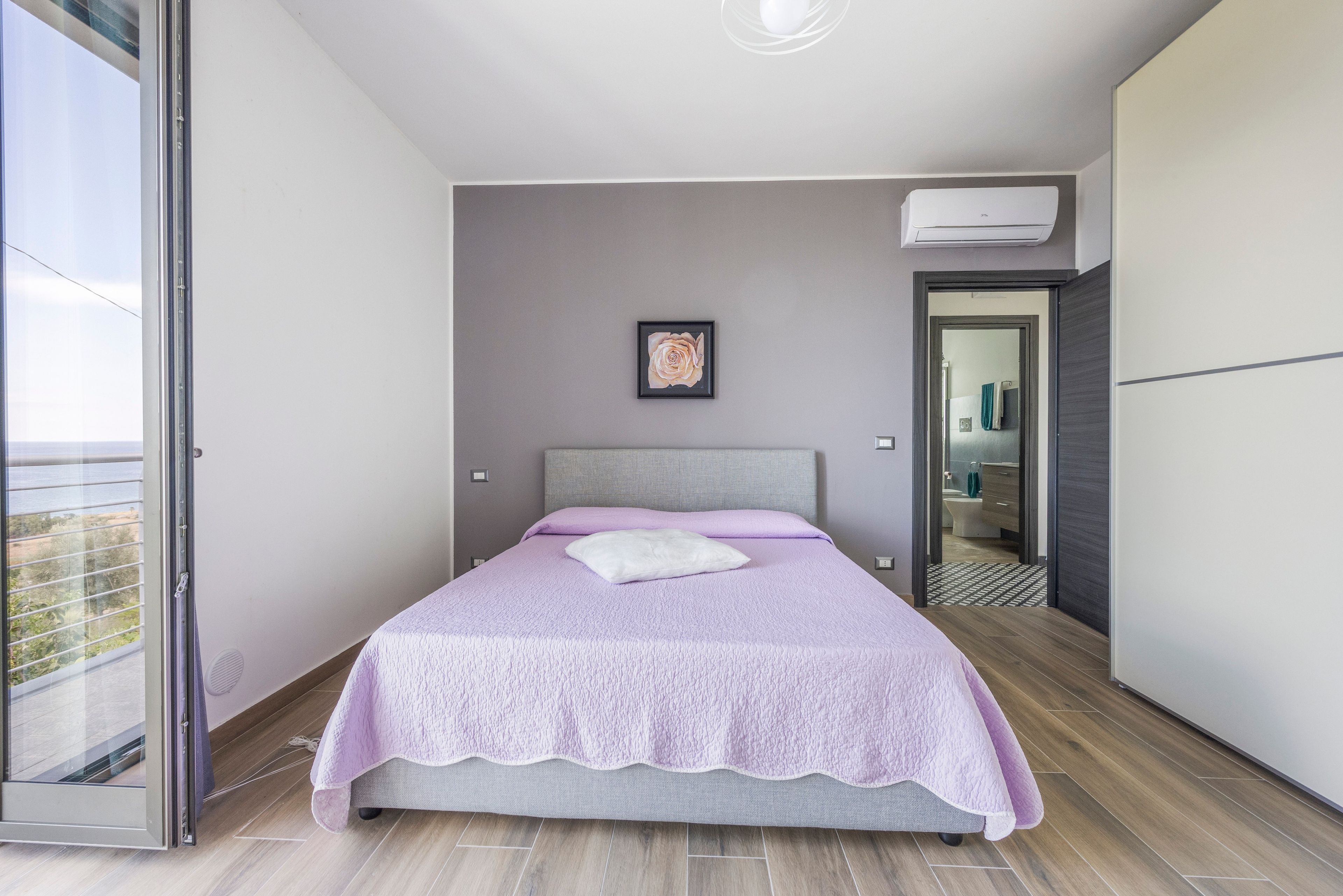 A bedroom with a bed, a picture on the wall, and a view through an open door.