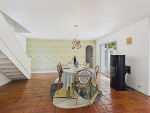 Un comedor con una mesa lista para cuatro personas, rodeada de sillas, un papel tapiz estampado y un televisor negro a la derecha.