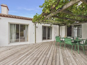 Una terraza de madera con pérgola, sillas verdes y una mesa.