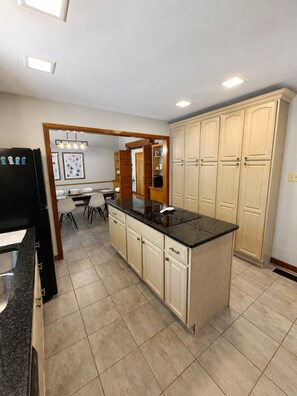 A kitchen with a central island, cabinets, and a dining area with chairs. - The Hunters Ridge Retreat (Chapel Hill)