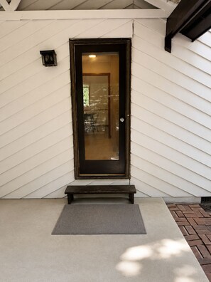 Une entrée de maison avec une porte vitrée à cadre sombre, un petit banc et un paillasson.