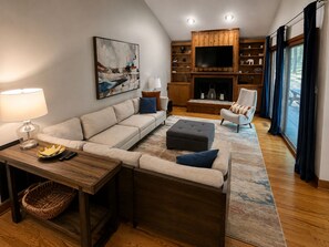 Un salon comprenant un canapé, un pouf et un fauteuil, une cheminée et un téléviseur.