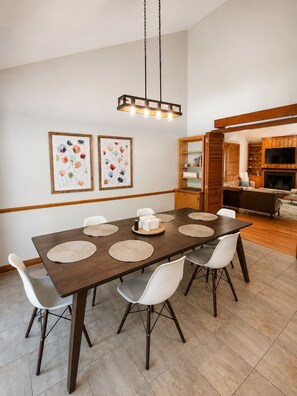 A dining area with a wooden table, white chairs, and a hanging light fixture. - The Hunters Ridge Retreat (Chapel Hill)