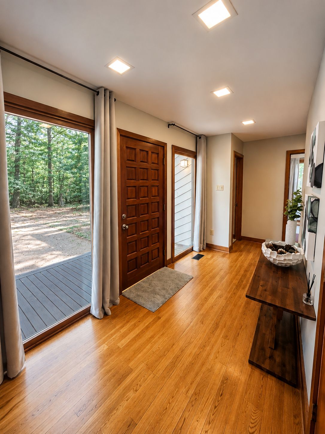 A wooden-floored hallway with a door, a rug, and a bench with a bowl.