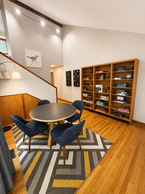 A room with a round table, blue chairs, a bookshelf, and a patterned rug. - The Hunters Ridge Retreat (Chapel Hill)