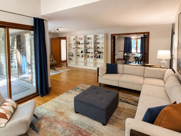 A modern living room with a sofa, ottoman, and a bookshelf filled with books and decorative items. - The Hunters Ridge Retreat (Chapel Hill)