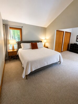 A bedroom with a large bed, two bedside tables with lamps, a window with curtains, a wardrobe, and a dresser. - The Hunters Ridge Retreat (Chapel Hill)