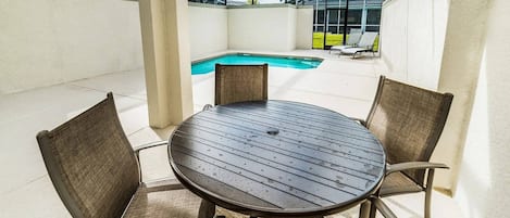Una mesa redonda con cuatro sillas en un espacio exterior techado, con una piscina al fondo.