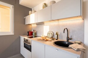 A modern kitchen with white cabinets, a black sink, and a countertop with a cutting board and a bottle of olive oil. - Dimora San Francesco - Seaview Terrace w/ Parking (Bari)