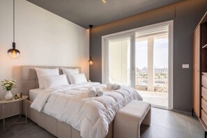 Una camera da letto con un letto grande, comodini, una panca, una finestra con vista e una porta che dà su uno spazio all'aperto.