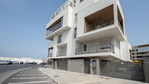 Un edificio residencial de varios pisos con balcones, entrada vigilada y cielo despejado.