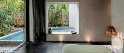 Un dormitorio moderno con un ventanal grande, vista a una piscina y una pared de piedra.