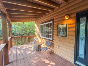 A wooden deck with a railing, two chairs, a lantern, and a window with a view of trees. - Cozy 2BR/2BA Helen Cabin for 4 | Hot Tub & Firepit (Sautee Nacoochee)