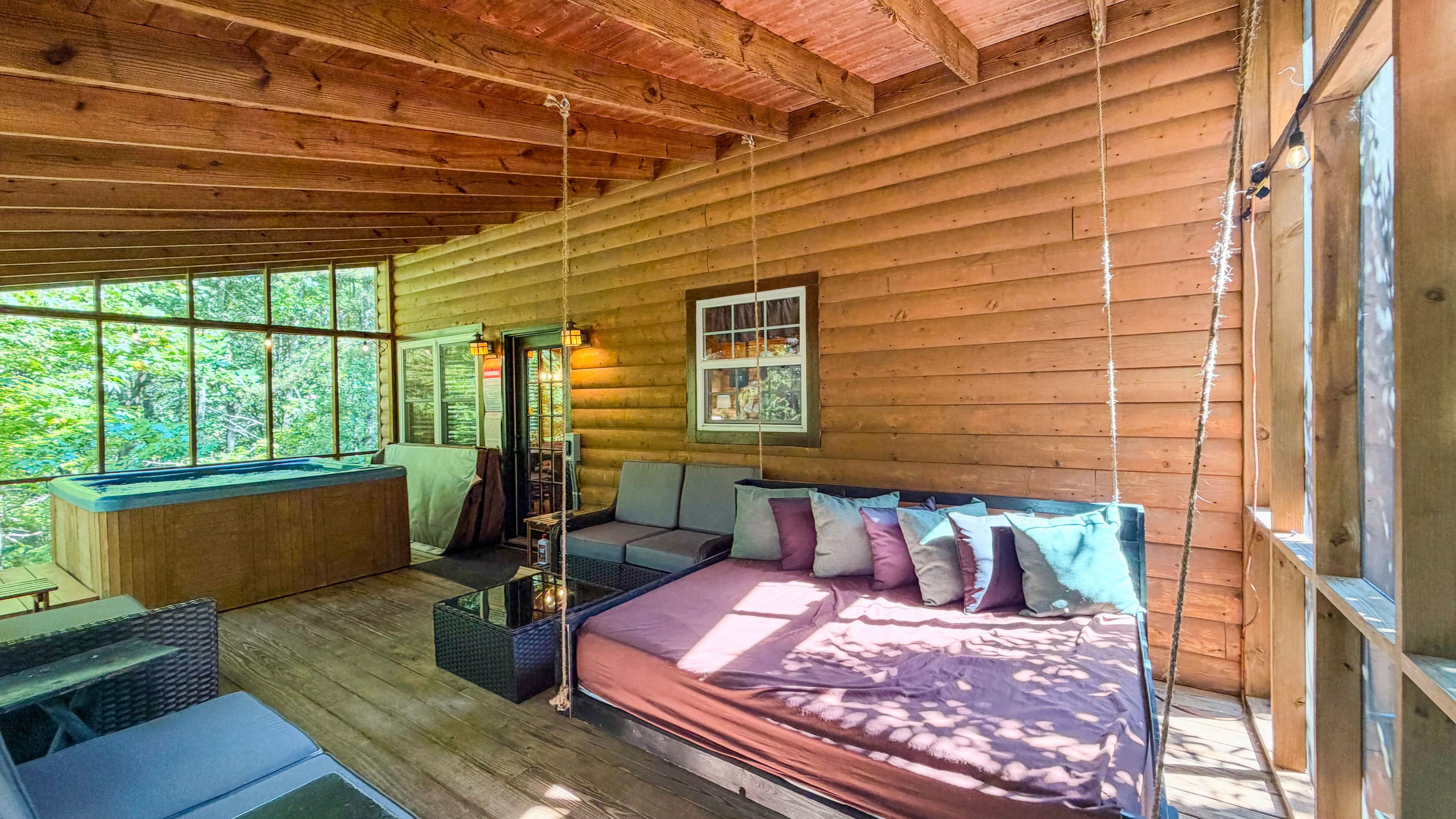 A cabin interior with a wooden floor, a bed with pillows, a sofa, a small table, and a hot tub.