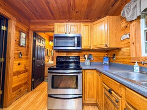 A compact kitchen with wooden cabinetry, a microwave, a stove, and a sink. - Cozy 2BR/2BA Helen Cabin for 4 | Hot Tub & Firepit (Sautee Nacoochee)
