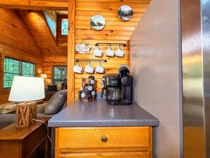A cozy cabin interior with a wooden ceiling, a coffee maker, mugs on a rack, and a 'Welcome' sign. - Cozy 2BR/2BA Helen Cabin for 4 | Hot Tub & Firepit (Sautee Nacoochee)
