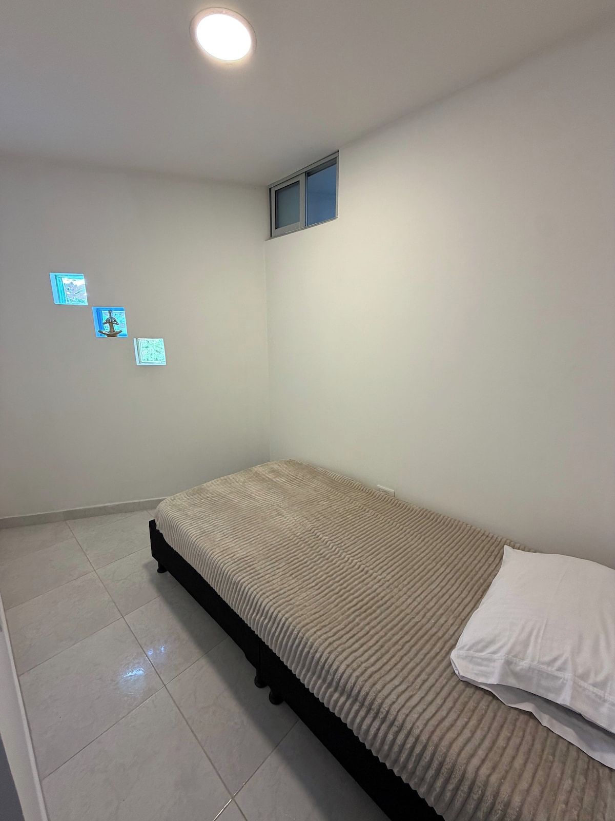 Quarto com uma cama de solteiro, uma janela pequena e uma luminária no teto.