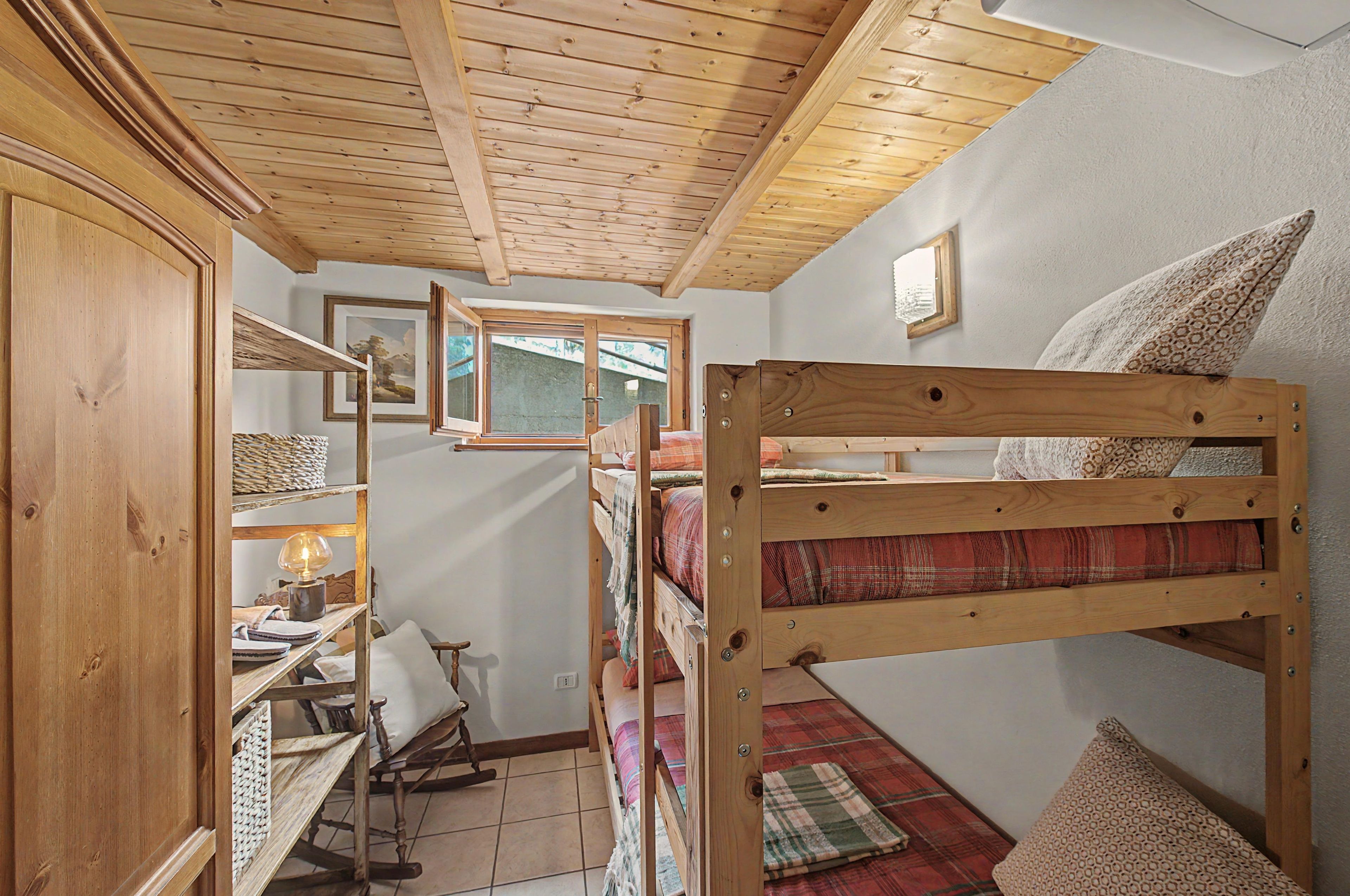 Una habitación compacta con una cama litera, estanterías de madera, un sillón mecedor y un escritorio pequeño con una lámpara.