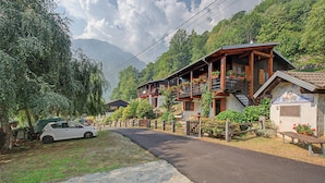 A traditional wooden chalet with a balcony, a stone pathway, and a car parked nearby.