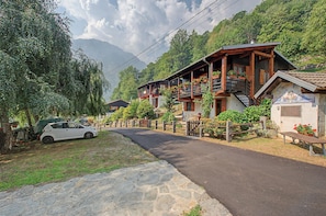 A traditional wooden chalet with a balcony, a stone pathway, and a car parked nearby.