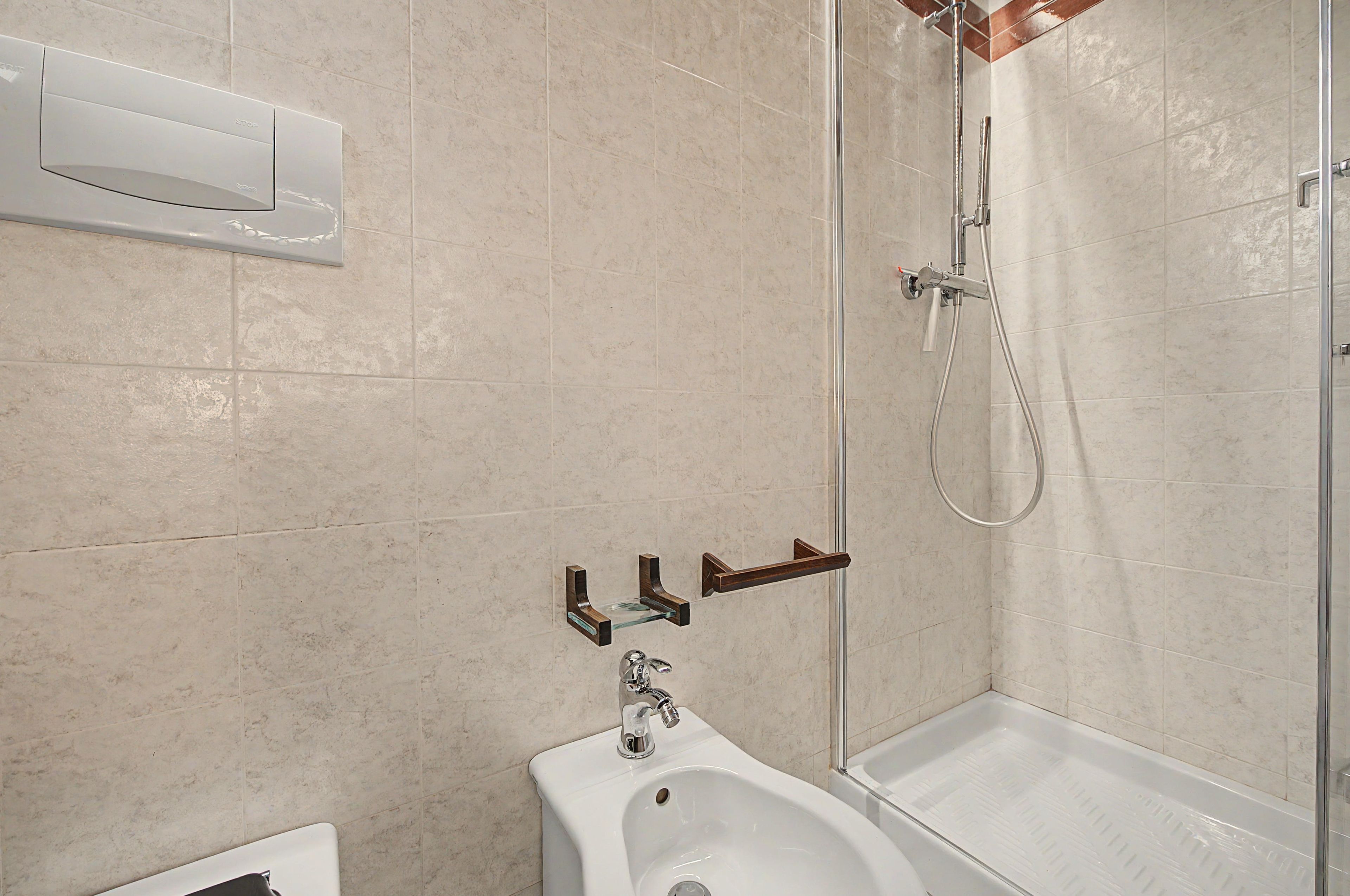 A modern bathroom with a glass shower enclosure, a white sink, and a bidet.