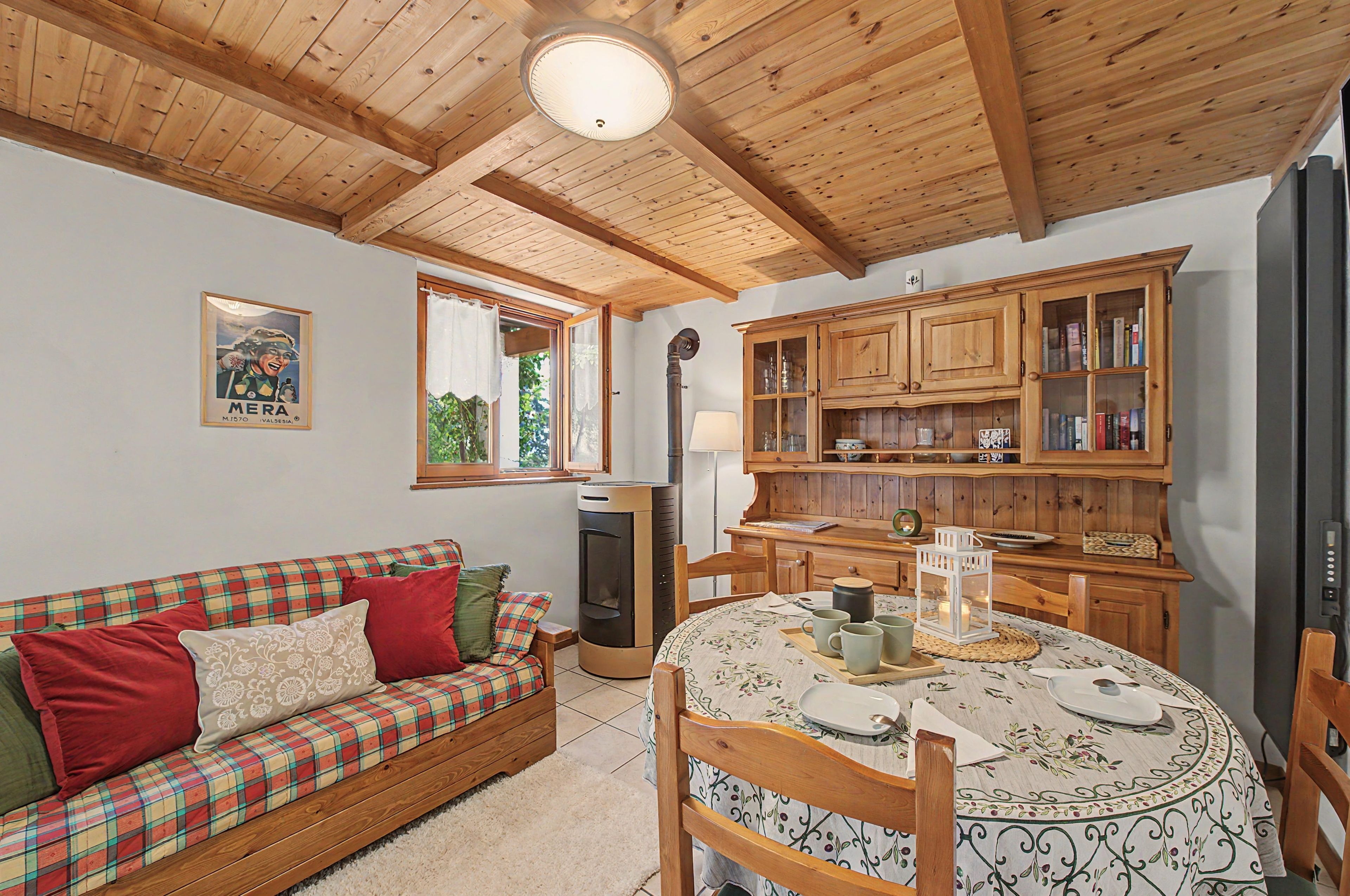 A cozy room with a wooden ceiling, a plaid sofa, a dining table with a floral tablecloth, and wooden cabinets.