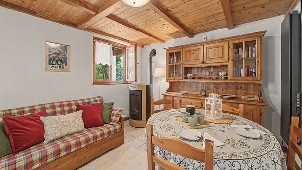 Ein gemütliches Zimmer mit Holzboden, einem Karosobensofa, einem Esstisch mit floralem Tischläufer und Holzschränken.