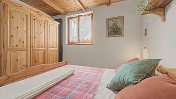 Une chambre avec une armoire en bois, un lit recouvert d’une couverture à carreaux et une fenêtre avec des rideaux.