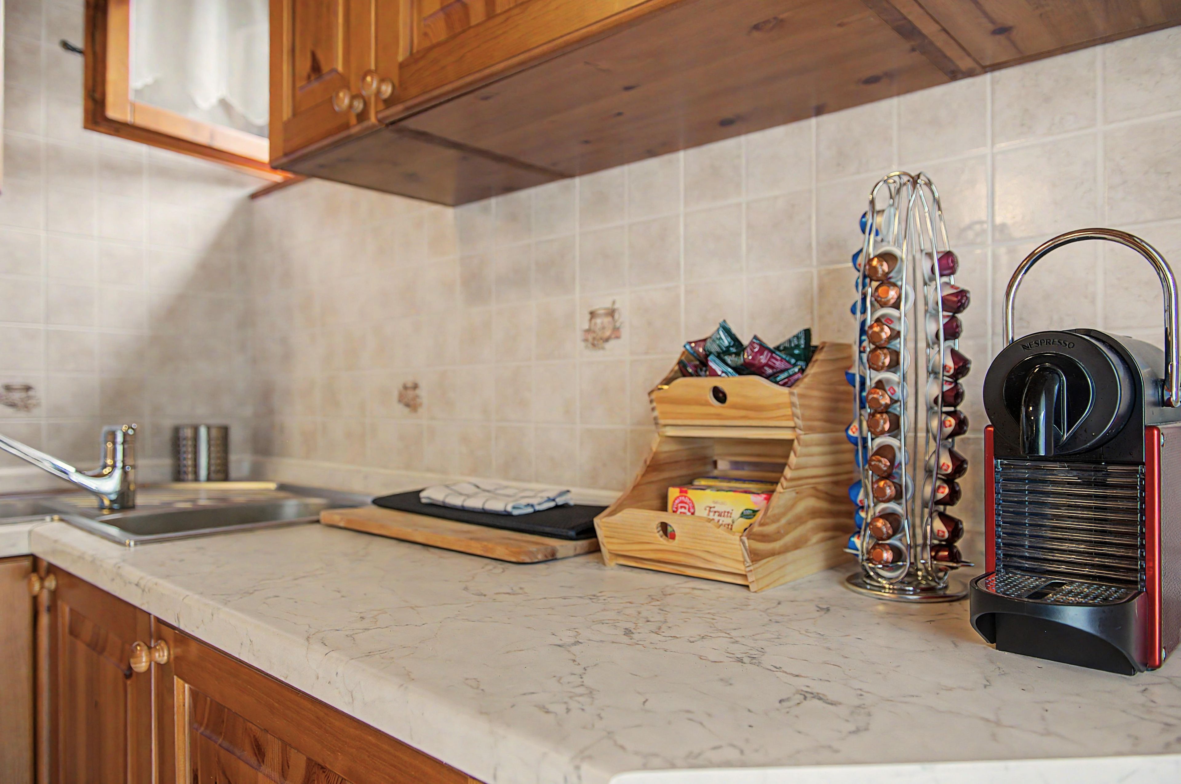 A kitchen with a marble countertop, wooden cabinets, a coffee machine, and a spice rack.