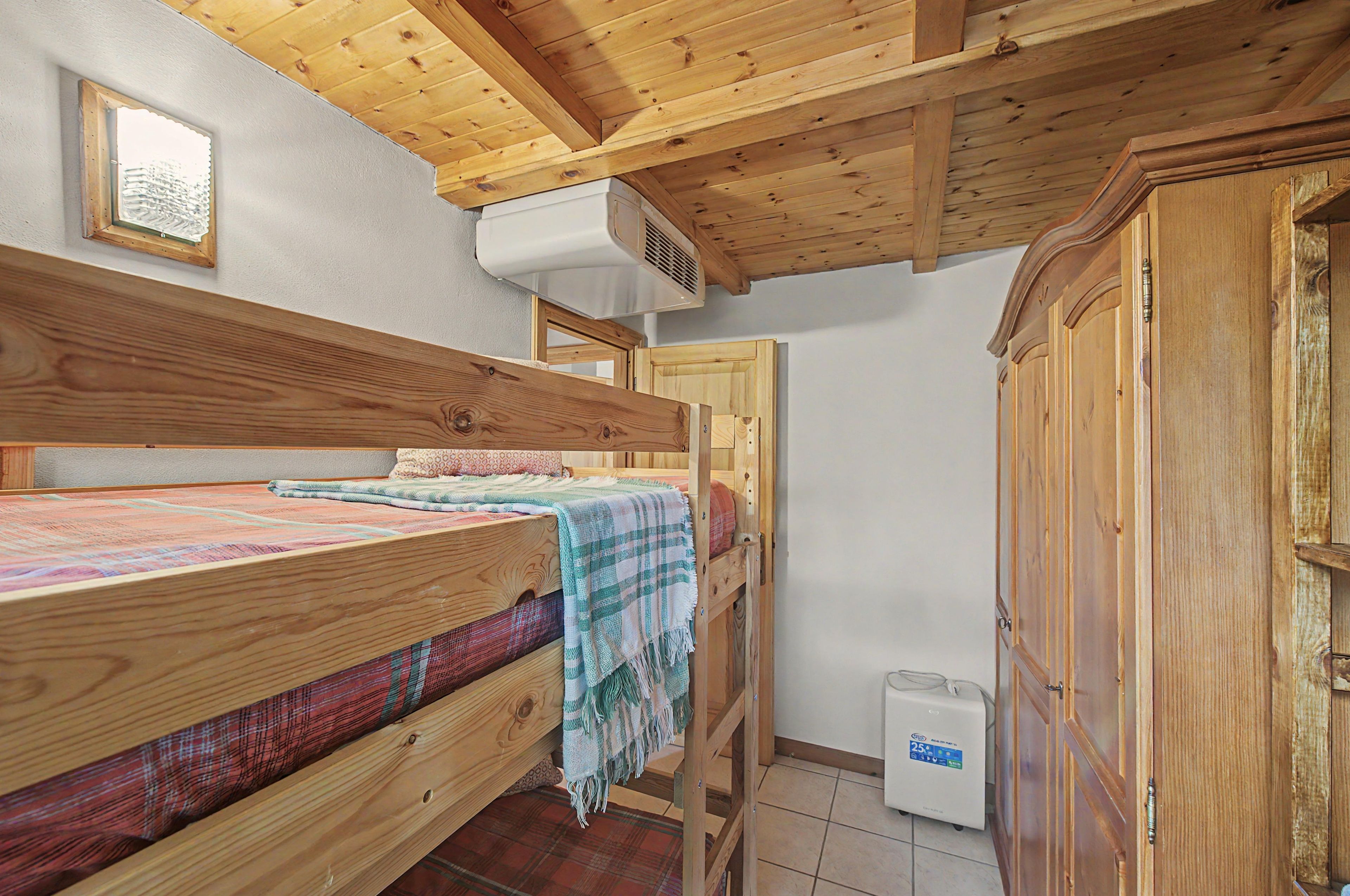 Een kleine, houten kamer met een stapelbed, een kledingkast en een verwarming.