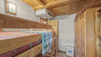 Een kleine, houten kamer met een stapelbed, een kledingkast en een verwarming.