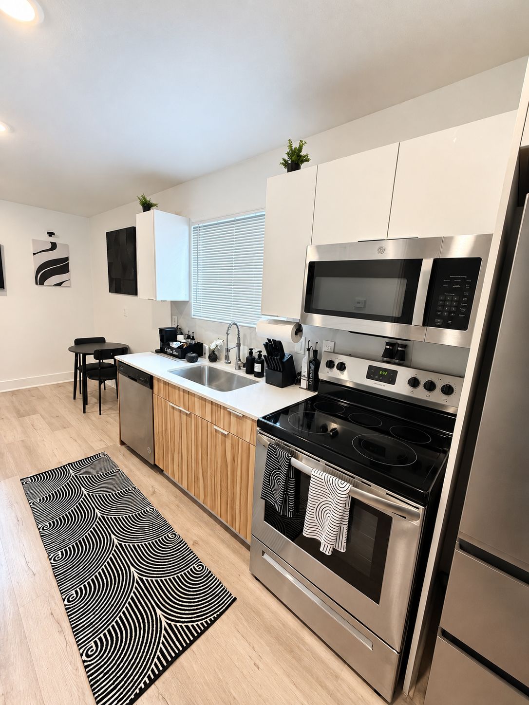 A modern kitchen with stainless steel appliances, a wooden countertop, and a black and white patterned rug.