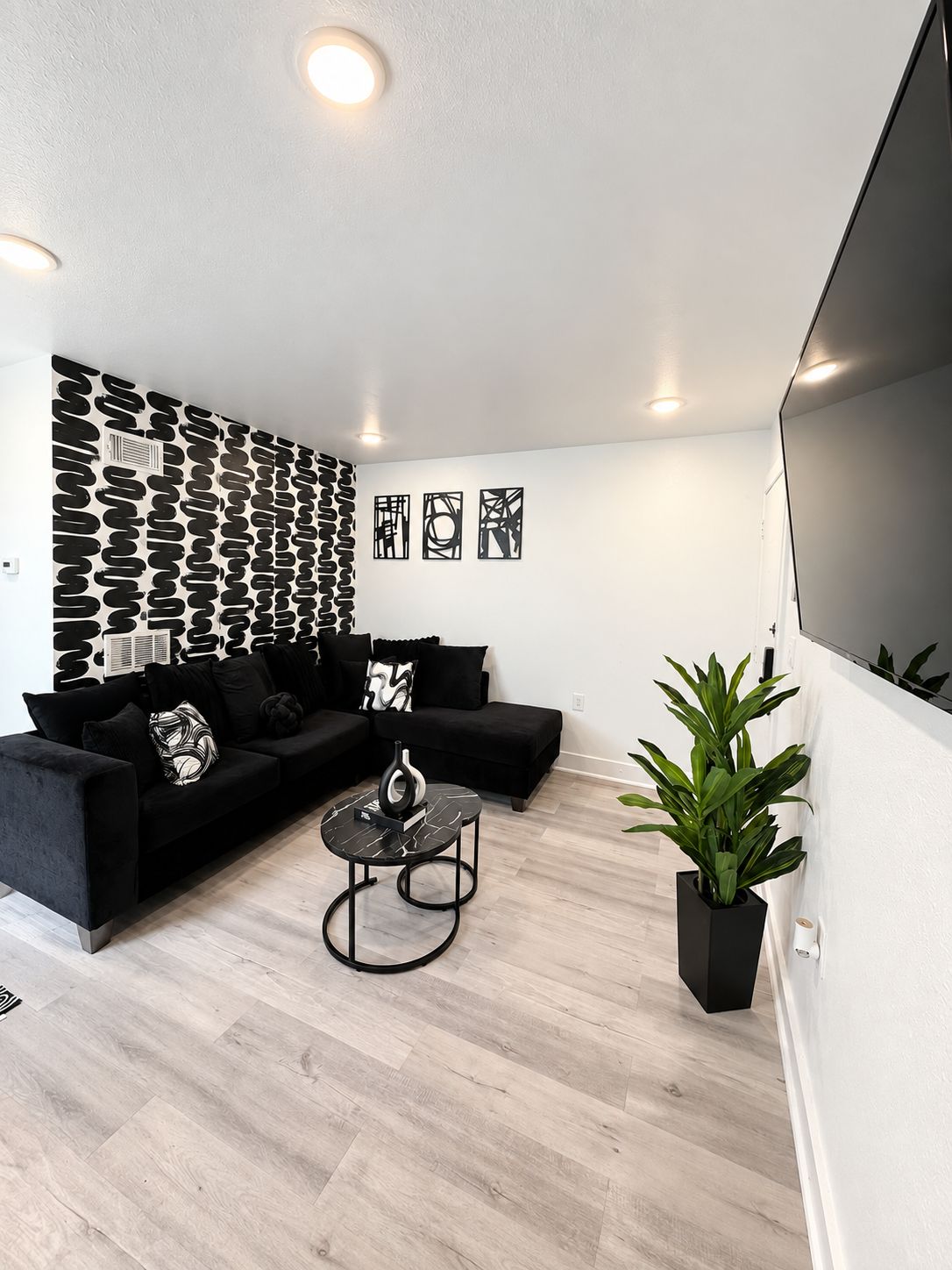 Una sala moderna con un sofá seccional negro, una mesa de centro redonda y una pared con estampado.