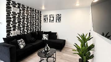 Una sala moderna con un sofá seccional negro, una mesa de centro redonda y una pared con estampado.