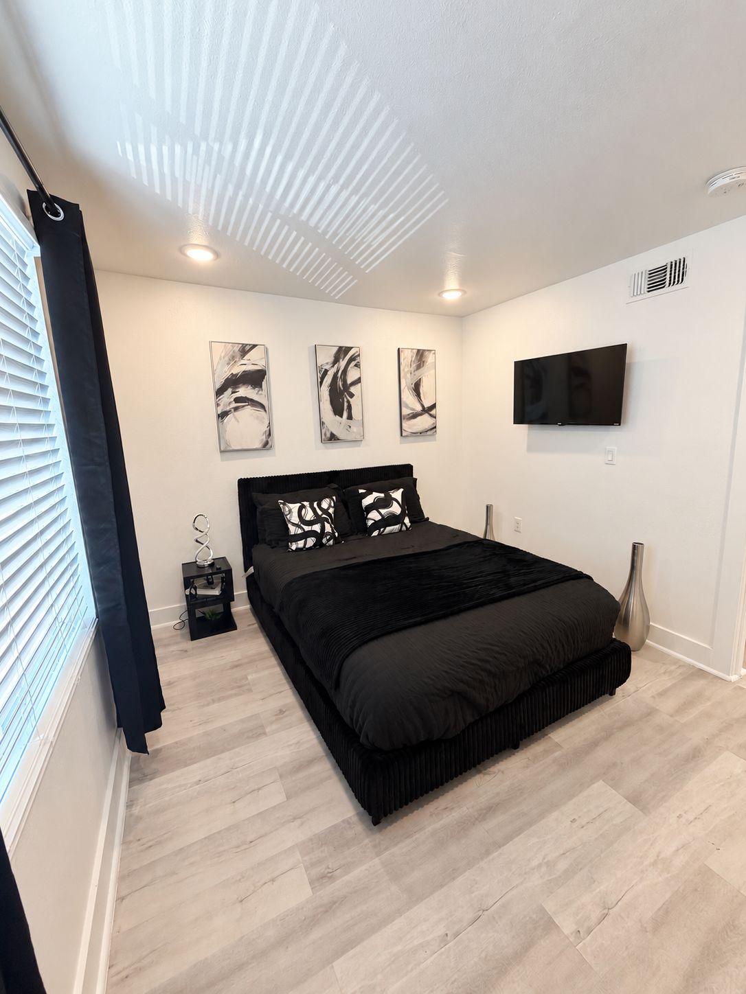 Une chambre à coucher moderne avec un lit, des œuvres d’art, une télévision et une petite table de chevet.