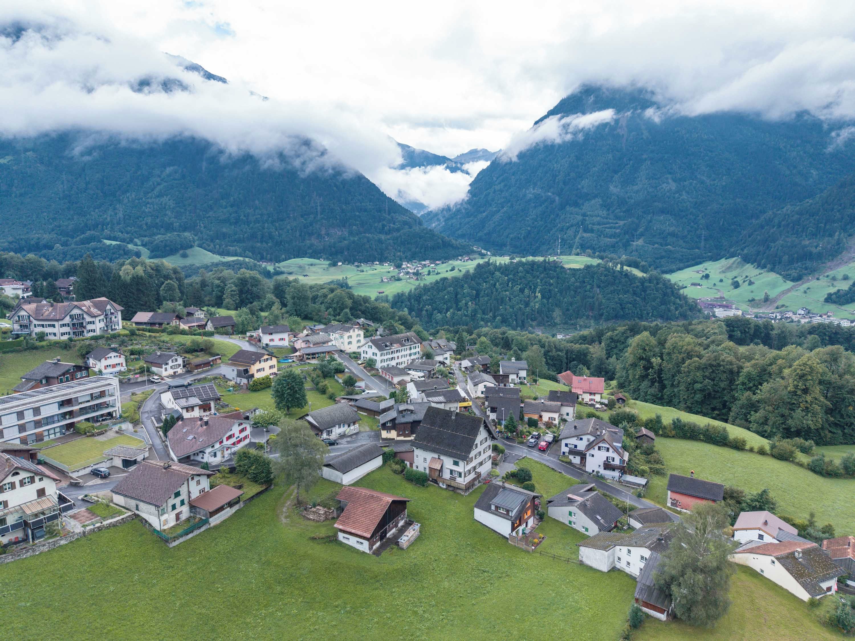 Ein Wohngebiet mit Häusern und Gebäuden, umgeben von Bergen und viel Grün.