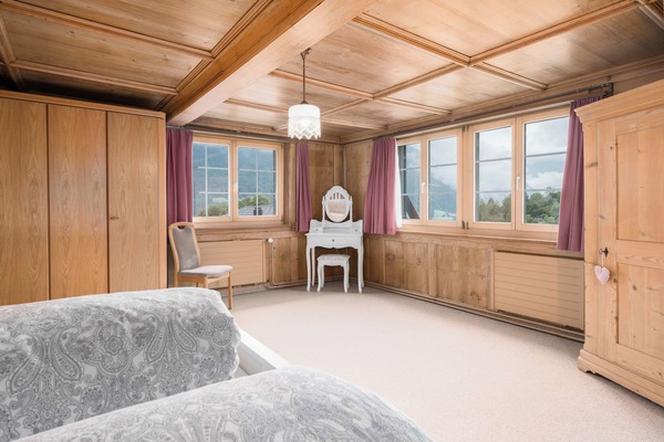 Bright private double room with warm wooden interiors, several windows, and a small vanity table, offering a cozy alpine atmosphere.