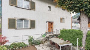 Un edificio blanco con balcón, una mesa con sillas y un pequeño jardín.