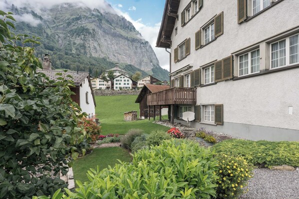A traditional chalet with a mountain backdrop, a well-maintained garden, and a clear view of the surrounding landscape.