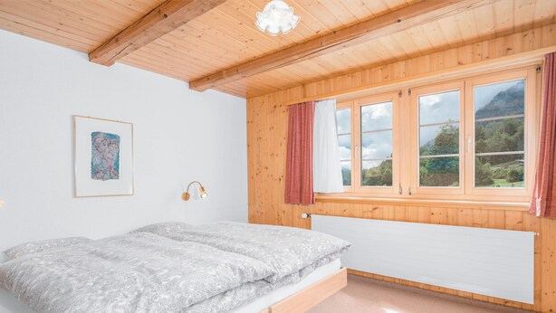 Un dormitorio con una cama, una ventana con cortinas, una lámpara de pared y un cuadro enmarcado.