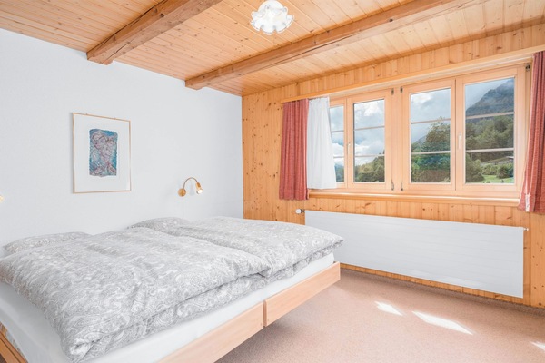 Bright private double room with several windows, warm wooden details, and views of the surrounding alpine scenery.