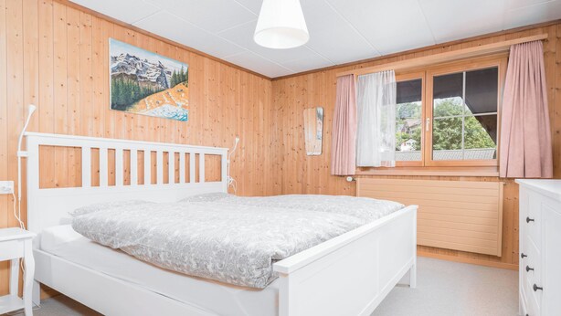 Un dormitorio con una cama blanca, paredes de madera, una ventana con cortinas y un cuadro en la pared.