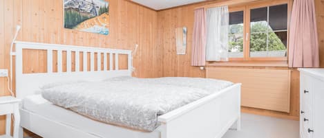 Un dormitorio con una cama blanca, paredes de madera, una ventana con cortinas y un cuadro en la pared.
