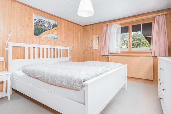 Bright private double room with several windows, warm wooden details, and views of the surrounding alpine scenery.
