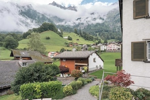 Vila rural com casas, um jardim e montanhas ao fundo.