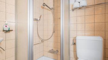 Un baño con ducha envuelta en vidrio, inodoro y repisa con artículos de aseo.