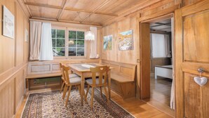 Un interior de madera con una mesa de comedor, sillas, un banco y vistas a través de una ventana.