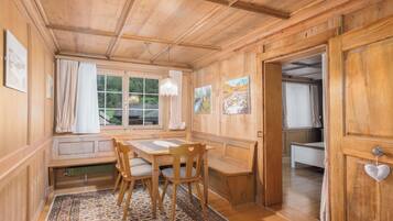 A wooden interior with a dining table, chairs, a bench, and a view through a window.